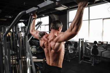 Spor salonunda barfiks çeken kaslı bir erkek sporcunun arka plan çekimi.