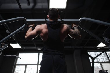 Spor salonunda barfiks çeken kaslı bir erkek vücut geliştiricinin düşük açılı çekimi.