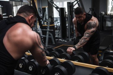 Parçalanmış erkek vücut geliştirici aynanın önünde dambıllarla egzersiz yapıyor.