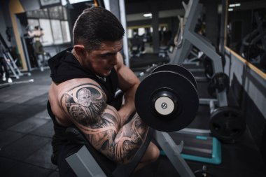 Spor stüdyosunda biseps yapan dövmeli vücut geliştirici.