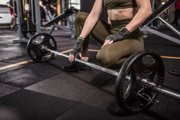 Unrecognizable sportswoman with fit body resting during barbell workout at gym