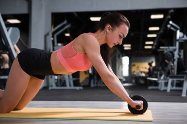 Güzel formda sporcu kadın spor salonunda kas tekeri üzerinde egzersiz yapıyor.