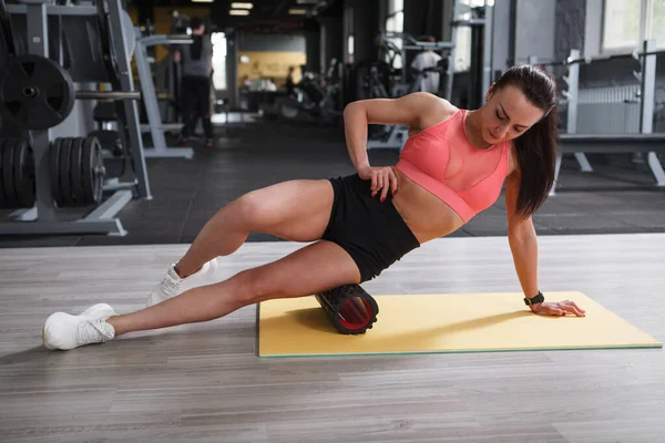 Spor salonunda köpük rulo üzerinde ağrıyan bacak kaslarına masaj yapan atletik bir kadın.