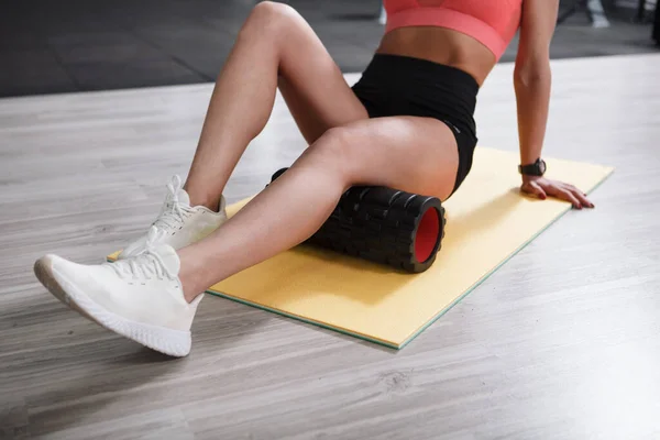 Tanımlanamayan fitness kadını spor stüdyosundaki köpük silindirde ağrıyan dizleri dikleştiriyor.