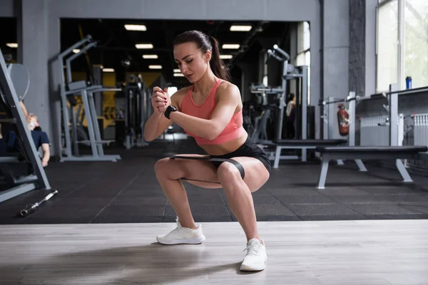 Fitness woman squatting at the gym, wearing resistance band on her legs