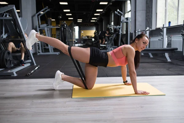 Athletic woman with fit body doing lower body workout with resistance band at the gym