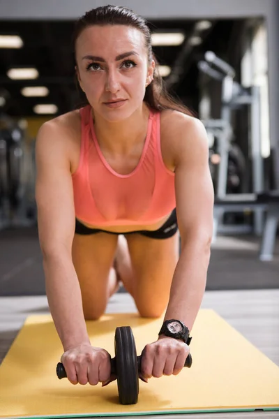 一名女运动员在体育馆用转轮加强其核心肌肉的垂直镜头 — 图库照片
