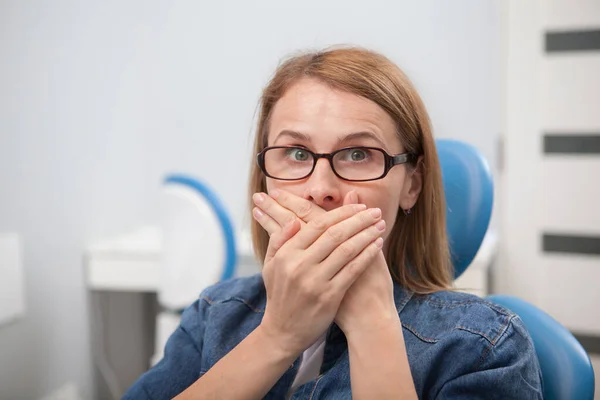 Przestraszona Kobieta Zakrywa Usta Dłońmi Siedzi Gabinecie Dentystycznym — Zdjęcie stockowe