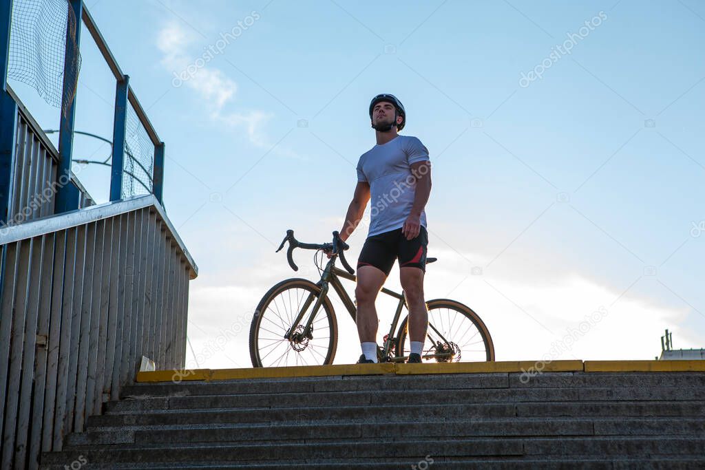 Low angle shot of a handsome athletic cyclist standing with his bicycle on top of the stairs in the city