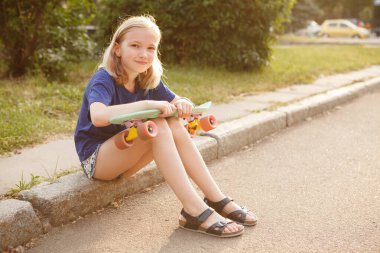 Sevimli genç kız neşeyle gülümsüyor. Pennyboard 'unda paten yaptıktan sonra dinleniyor.