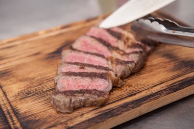 Şef ahşap kesme tahtasıyla orta pişmiş biftek kesiyor.