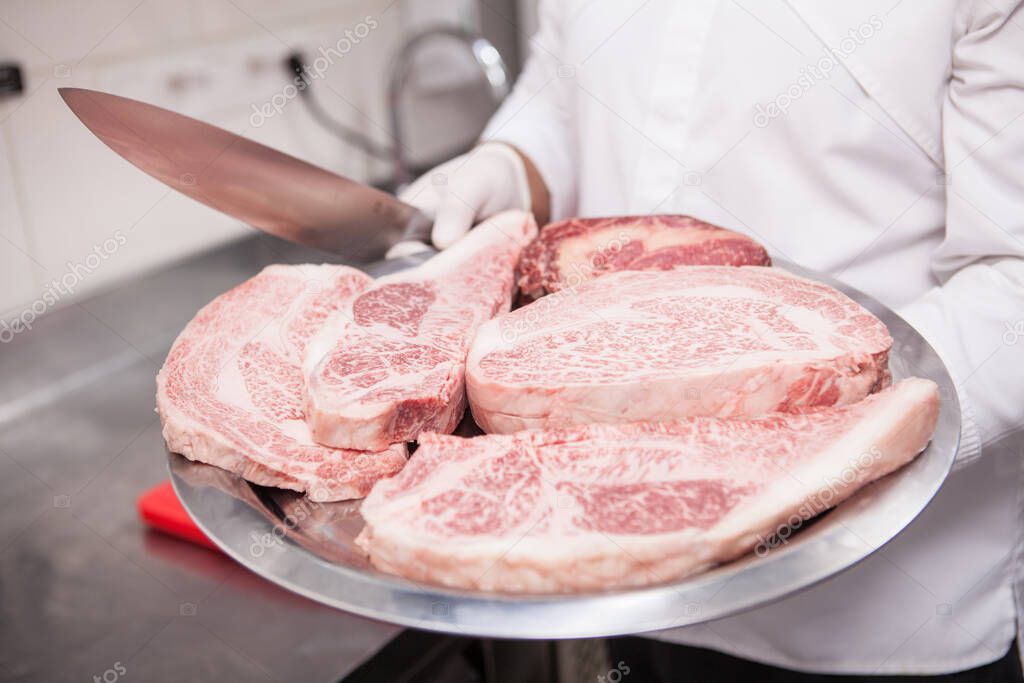 Cropped shot of a chef holding plate full of marbled beef meat