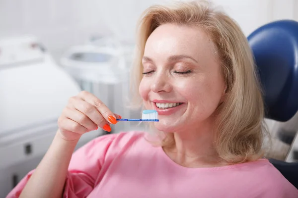 Happy mature woman smiling with eyes closed, holding toothbrush with toothpaste