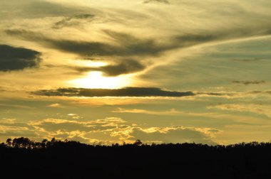 Yoğun bir orman bölgesinin ardında batan bir güneşin resmi. Ardından dağlar..