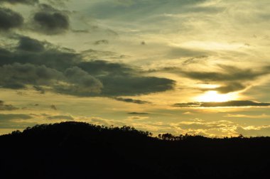 Güneş sık bir ormanın arkasında batıyor ve ardından dağlar geliyor..
