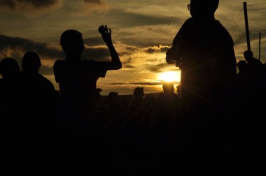 Yoğun bir orman bölgesinin ardında batan bir güneşin resmi. Ardından dağlar..