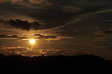 Güneş sık bir ormanın arkasında batıyor ve ardından dağlar geliyor..