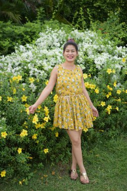 Bahçede sarı çiçeklerle poz veren Asyalı kadın.