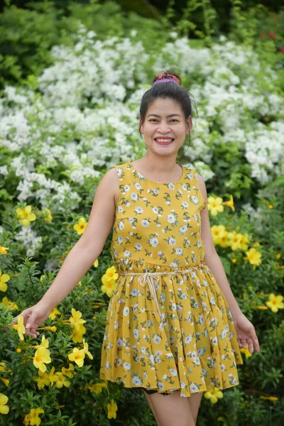 庭で黄色の花にポーズアジアの女性 — ストック写真