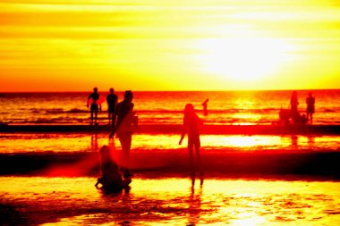 Gün batımında sahildeki insanların silueti.