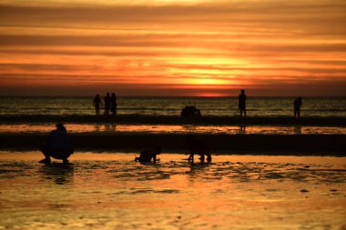 Gün batımında sahildeki insanların silueti.