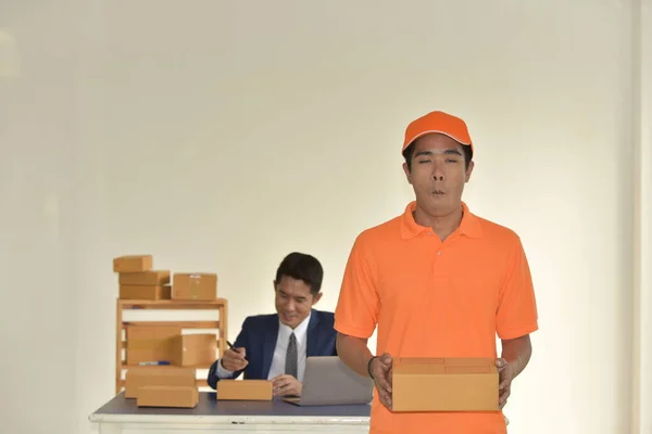 Delivery worker with cardboard box with businessman working at table on background