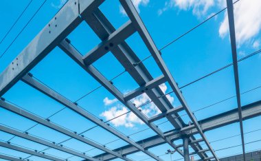 Metal beam structural framework creating a systematic geometric grid, emphasizing modern engineering and architectural design against a clear blue sky with white clouds