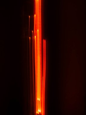 Abstract light trails creating vibrant vertical orange and red streaks on a dark background, representing energy, movement, data flow, and modern technology