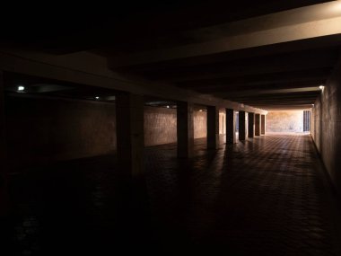 Dark urban underpass with concrete pillars leading towards a brightly lit exit, representing concepts of hope, progress, the way out, and moving from shadow into opportunity