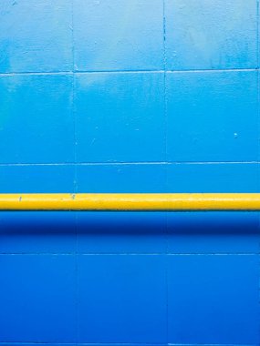 Parlak sarı bir yatay korkuluk veya güvenlik bariyeri içeren kalın mavi duvar, çarpıcı bir kontrast ve açık çizgiler ve birincil renkler içeren minimalist grafik arkaplan oluşturur