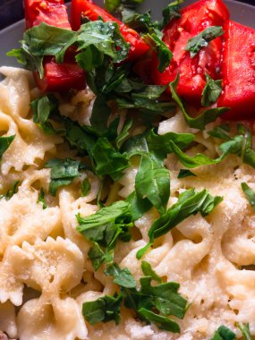 Farfalle pasta swimming in a light cream sauce, generously topped with vibrant red fresh cut tomatoes and scattered green arugula leaves, showcasing a balanced and flavorful Italian dish