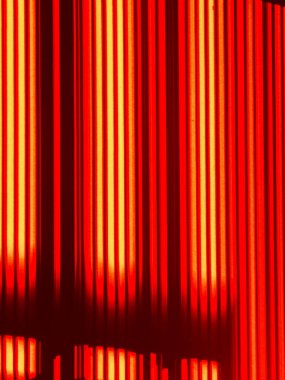 Yüzeyden yansıyan parlak sıcak ışık, dikey kırmızı ve turuncu çizgilerle karanlık bir arkaplan oluşturarak enerji ve modern tasarımı çağrıştırıyor.