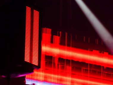 Parlak kırmızı LED paneller ve lazer ışınları, yüksek enerjili canlı müzik performansı ortamı için canlı desenler ve elektrik parıltısı oluşturan karanlık bir konser sahnesini aydınlatır.
