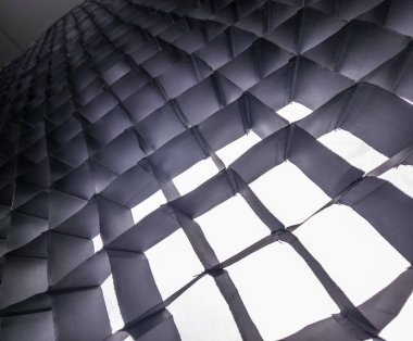 Kumaş ışık dağıtıcı farklı kare hücrelerle geometrik ızgara deseni oluşturarak gölgelerin soyut bir dokusu ve tek renkli renklerde vurgular oluşturur.