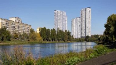 Berrak bir sonbahar gününde açık mavi gökyüzü altında eski Sovyet döneminden kalma apartman binalarıyla modern gökdelenler arasında uzanan, yemyeşil kıyılar arasında akan sakin bir nehir manzarası.