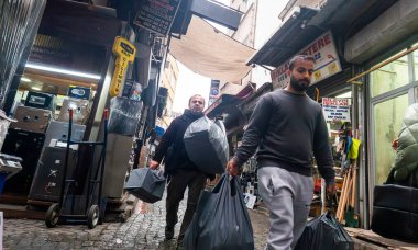 İstanbul, Türkiye - 8 Aralık 2025, İstanbul, Türkiye 'nin geleneksel pazar bölgesinde dar ve hareketli bir sokakta alışveriş torbaları taşıyan erkekler