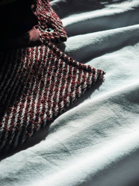 Herringbone desenli kumaş karmaşık dokuma ve dokuyu gösteriyor. Kırışık tekstil yüzeyiyle çelişiyor. Güneş ışığıyla aydınlanıyor ve güçlü gölgeler yaratıyor.