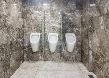 Minimalist umumi erkekler tuvaletinde üç beyaz pisuvar mermer duvarlara ve fayanslı zemin, modern, temiz ve hijyenik tesislere karşı buzlu cam bölmelerle ayrılmış.