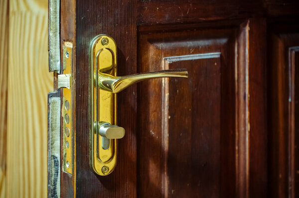 Damaged wooden door featuring a dislodged golden handle and visible lock mechanism, conveying concepts of security breach, home invasion, or repair needs