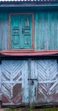 Eski ahşap bir binanın yıpranmış ön cephesinde soluk mavi renkli garaj kapılarının üzerinde paslı asma kilit, çürüme ve klasik cazibe kavramlarını yansıtan soluk mavi bir kapı görülüyor.