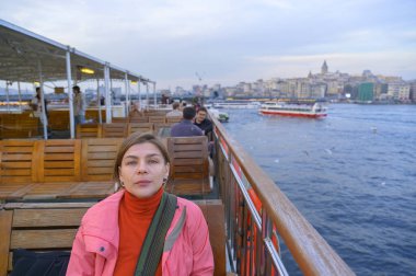 İstanbul ufuk çizgisini ve Galata Kulesi 'ni seyreden, gezerken dinlenen, tarihi liman ve şehir manzaralarını seyreden, İstanbul feribot yolculuğunun keyfini çıkaran bir kadın.