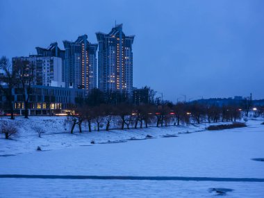 Kyiv 'in modern apartmanları, akşam saatlerinde karla kaplı nehir ve donmuş Dinyeper nehri aydınlatacak mavi kış alacakaranlık gökyüzüne karşı dimdik ayakta duruyor.