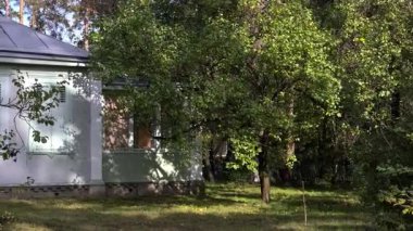 Güneş ışığı, yeşil bir bahçedeki kırsal bir evin duvarına hareket eden ağaç gölgelerini düşürüyor.