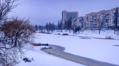 Kyiv 'de soğuk bir kış günü, konut binaları ve kısmen donmuş bir nehirle karlı bir şehir manzarasının üzerinde yükselen Ukrayna ana anıtı