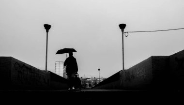 Kyiv, Ukrayna - 12 Mayıs 2022: Şemsiyeli siluetli banliyö işçisi, alacakaranlıkta kasvetli bir şehir caddesinde yürüyor, yüksek kontrastlı şehir manzarası ve grafitiye karşı tek başına bir fiği var