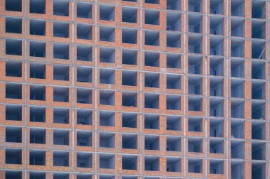 Boş pencere çerçeveleri inşaat halindeki tuğla ve beton bir bina üzerinde şebeke deseni oluşturuyor, kentsel gelişimi, konutları ve yeni mimarinin yapısal iskeletini yansıtıyor