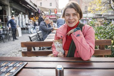 İstanbul 'da şehir hayatı ve konukseverliğin tadını çıkaran yalnız bir bayan gezgin, bir sokak üzerindeki açık bir kafede dost canlısı bir mahalle kedisiyle bir an için mola veriyor.