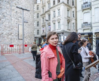 Kırmızı ceketli bir kadın hareketli bir İstanbul caddesinde duruyor, kameraya bakıyor, tek başına seyahat ediyor ve arka planda tarihi Galata Kulesi ile şehrin kentsel çevresini keşfediyor.