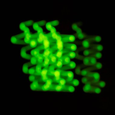 Yeşil ışık çizgileri ve bokeh, siyah bir arkaplan karşısında, teknolojiyi, veriyi veya canlı bir dijital konsepti temsil eden soyut, dinamik bir model oluşturur.
