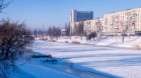 Donmuş Dinyeper Nehri Ukrayna 'nın başkenti Kyiv' e akar, açık bir kış gökyüzü altında karlı toprak setinin altındaki apartmanları yakalar, uzak kentsel mimariyi gösterir.